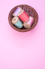 Fototapeta na wymiar basket with multicolored cotton spools on a pink background