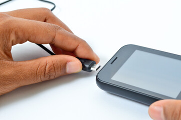 Charging a smartphone via a USB cable and a power supply on a white background. Silhouette of a black smartphone hanging with a usb charging cable on a white background