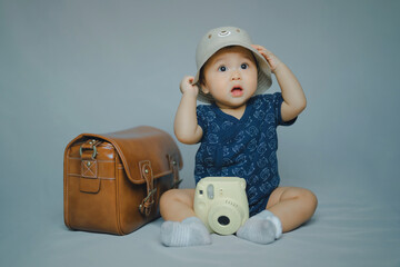 portrait of baby in blue dress and hat in concept learning and development in dream with play camera toy and vintage bag