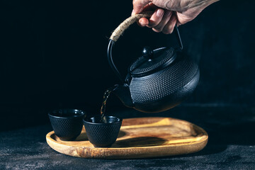 Hand holds a black kettle and pours tea into a mug, low key