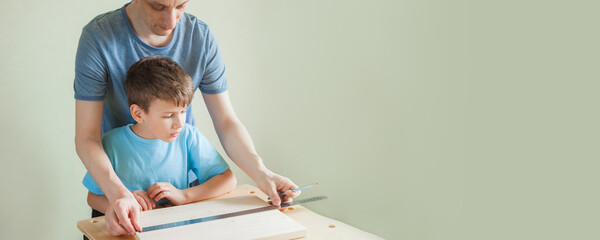 Father teaches son carpentry. Cute little boy looks how to make marks on wooden plank. Banner with copy space