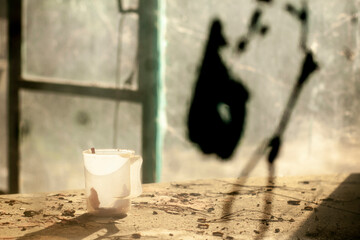 A still life image with an old plastic mug on a devastated table. Plastic mug with a hard shadow in...