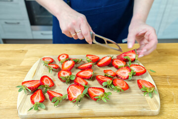 A close up of a girls hands holding a knife and preparing fruit by slicing strawberries on the wooden board at home