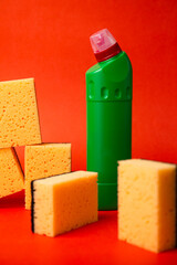 A bottle of detergent with cleaning sponges on a red background