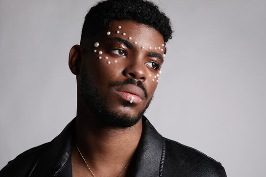 Close-up of handsome black man with pearls on his face. Isolated on white wall.