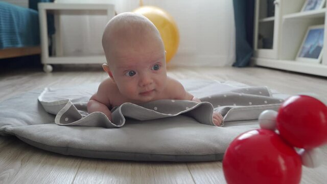 Tummy time for babies, father helps baby learn head control, 3 month old baby boy lying on stomach on activity play mat at home. High quality 4k footage