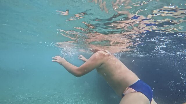 Underwater View. The Boy Dives and Swims in the Transparent Sea Water. Movement in Water on Stones. Sun Glare.