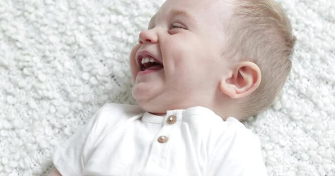 Baby boy lying on his back laughing because getting tickled on his belly, close up slowmotion handheld