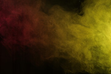 Artificial magic smoke in red-yellow light on black background
