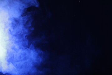 Artificial smoke in blue light on black background