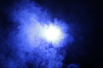 Artificial magic smoke in blue light on black background