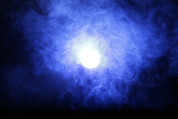 Artificial magic smoke in blue light on black background