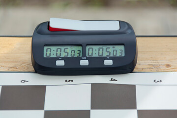an electronic chess clock stands on a wooden table, next to the chessboard.