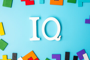 IQ text with colorful wood puzzle pieces, geometric shape block on blue background. Concept of intelligence quotient and logic thinking