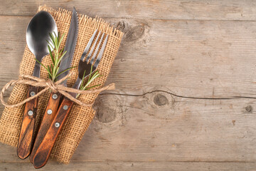 Spoon, fork, and knife along with linen napkin on the wooden background, retro style. Dining set.