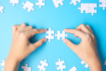 hands connecting couple white puzzle jigsaw pieces on blue background. Concept of solutions, mission, success, goals, cooperation, partnership, strategy and puzzle day