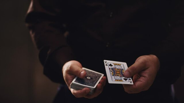 Magician illusionist showing performing card trick. Close up of hand and poker cards on black background.