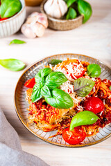 Italian pasta with tomato sauce, tomatoes, cheese and basil on a light table, vertical photo