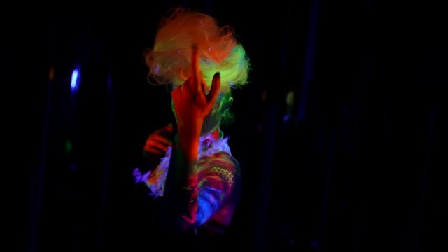 actress with fluorescent makeup and body art is moving in darkness, theatrical performance