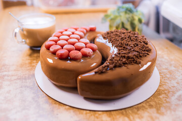 On an old wooden table there is a beautiful chocolate cake, a transparent cup with coffee and a small plant