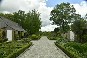 Fototapeta na wymiar L'allée d'accès en pierres avec ses parterres de fleurs et coins de repos à l'arboretum de Wespelaar en Brabant Flamand 