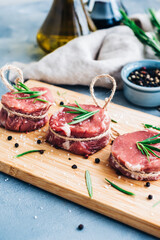 Raw beef filet mignon steak on a wooden board with rosemary and spices.