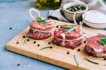 Raw beef filet mignon steak on a wooden board with rosemary and spices.