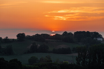 A warm sunset over the rolling hills in the south of Limburg near Maastricht. The last sunbeams give a golden colour over the hills and the field with wild yellow orchids.