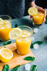 Female bartender cooking fresh lemonade with mint and lemon in glass with ice.