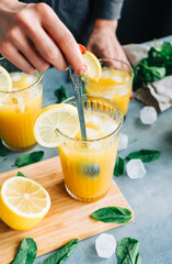 Female bartender cooking fresh lemonade with spoon in glass with ice.