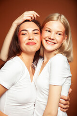 two pretty diverse girls happy posing together: blond and brunette, caucasian and asian on brown background, lifestyle people concept