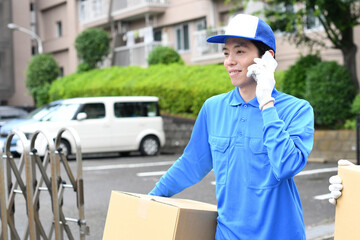 作業服を着た男性が引っ越しの段ボールを運びながら電話をするイメージ