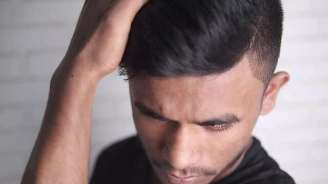 side view of man styling hair with comb on black background,