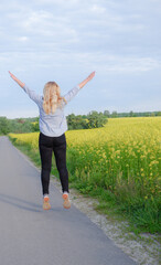 Rear view of a happy girl jumping against the background of a blooming rapeseed field. Bright yellow rapeseed flowers in the rays of the sunset.