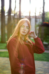 Street portrait of a young red haired woman with transparent sunglasses during a golden hour, backlight