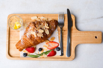 Fresh French croissants with strawberry ripe berries on cutting wood board background.