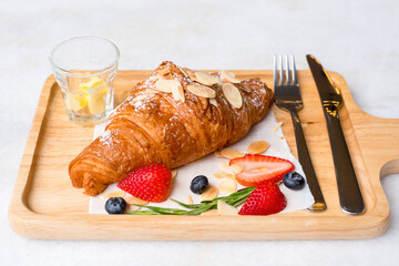 Fresh French croissants with strawberry ripe berries on cutting wood board background.