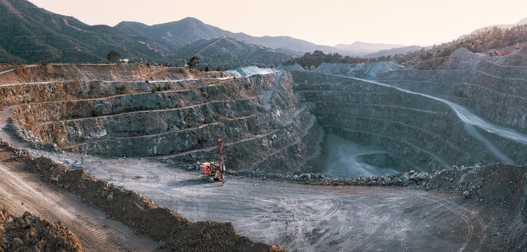 Gravel quarry with terraces, piles of stone and red crusher machine. Panorama with mountains background in twilight