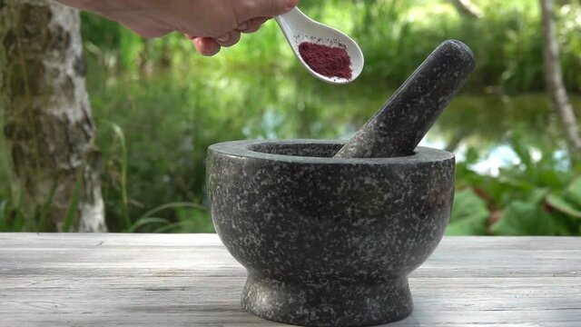 Hand is putting fresh spices into the grey stone mortar in slow motion outdoors