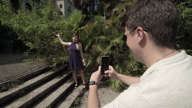 the guy takes pictures of his happy girlfriend against the background of bright green bushes 