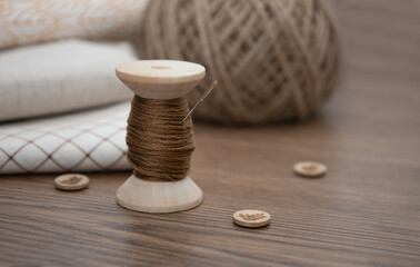Fototapeta na wymiar A spool of thread,a needle, and buttons on a wooden table. Sewing supplies