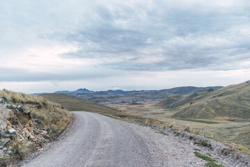 dirt road in the Andes of Peru with a blue sky and gray clouds at sunset surrounded by straw from the mountains