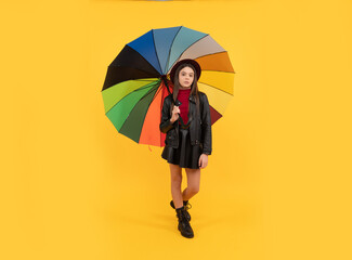 happy teen girl in hat and leather clothes under rainbow umbrella, rainy autumn