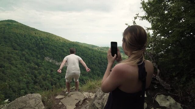 the girl takes pictures of her boyfriend on the camera against the backdrop of a beautiful landscape 