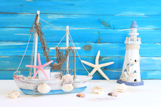 nautical concept with white decorative sail boat, seashells over wooden table and blue background