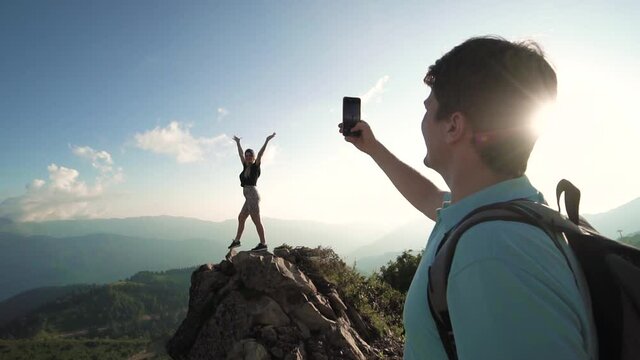 husband takes pictures of his wife against the backdrop of large mountains and sunset Sochi