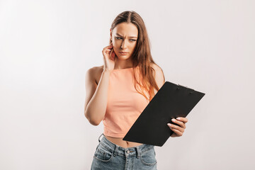 Girl student frowns with displeasure and reads information in documents. Beautiful young business woman holds a clipboard with mockup on gray background. Study and business concept. Online learning