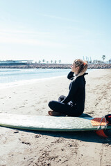 Vertical shot of a girl sitting on the beach with a surfboard.