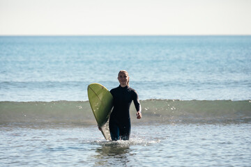 Young girl coming out of the sea with a surfboard.