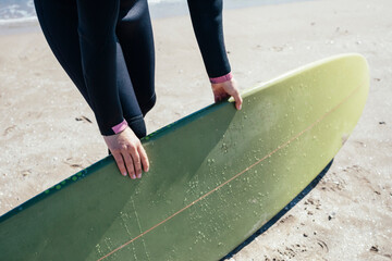 Close up shot of girl hands holding a surfboard on the beach. Summer and vacation concept.